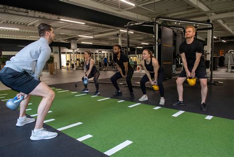 Groep tieners onder begeleiding van een trainer die correcte fitnessoefeningen uitvoeren.